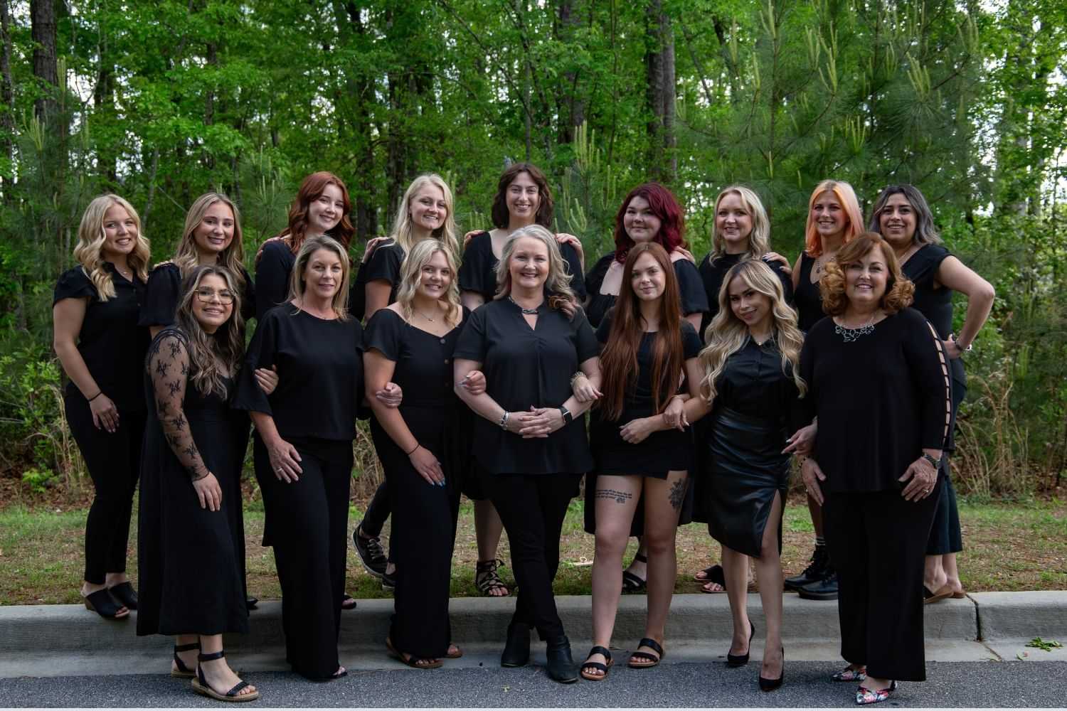 Group of women in black outfits posing together outdoors in a forested area.