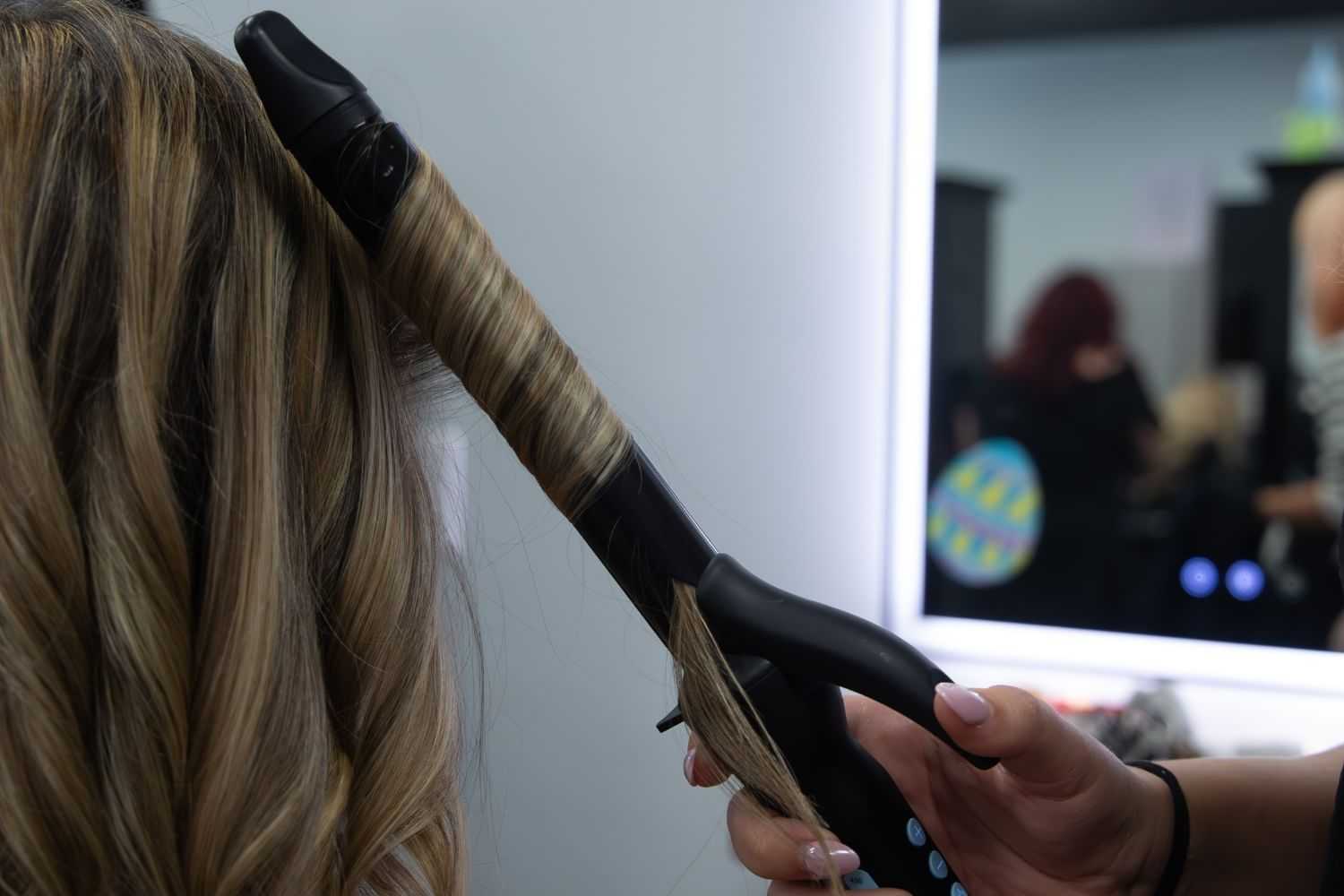 Hairdresser using curling iron on client's blonde hair in salon setting.