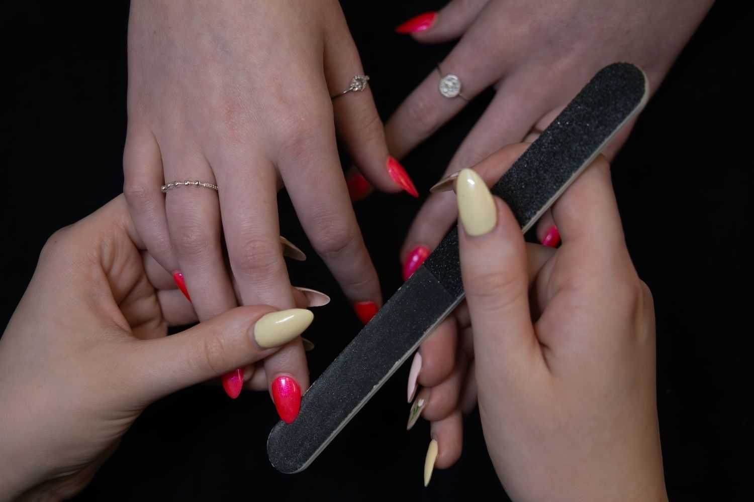 Manicure process with red and beige nails being filed.