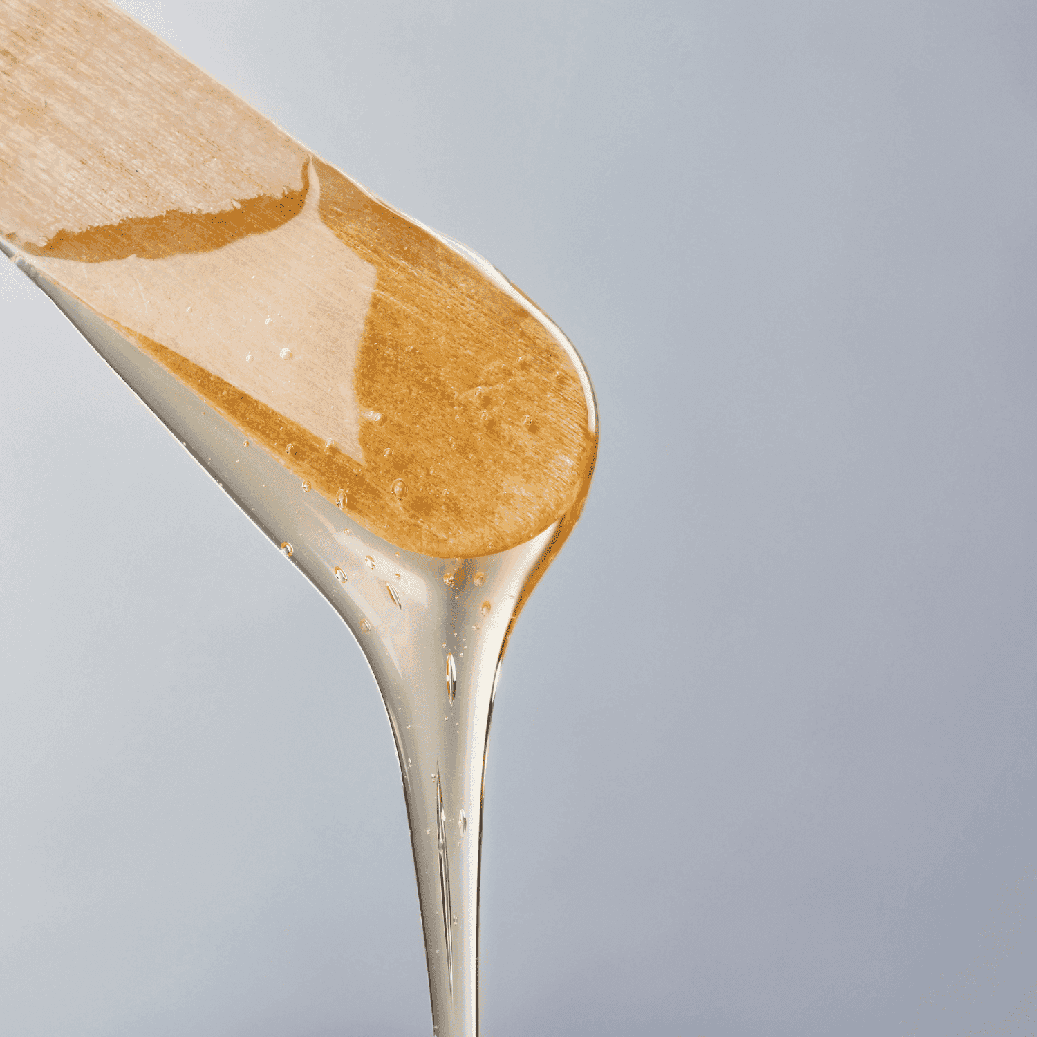 Hot wax dripping from wooden spatula against a gray background.