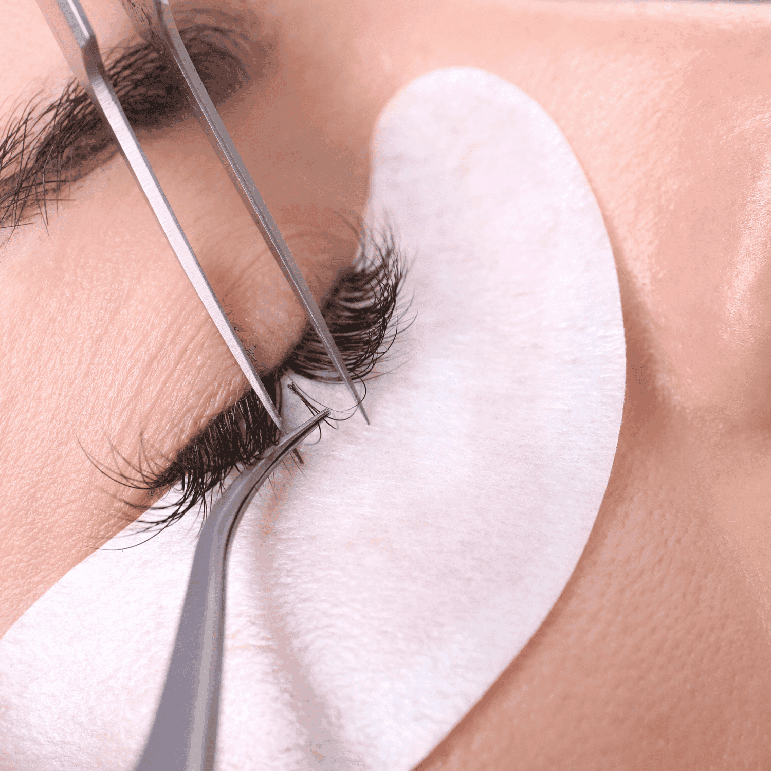 Applying eyelash extensions with tweezers on closed eye, protective pad underneath.