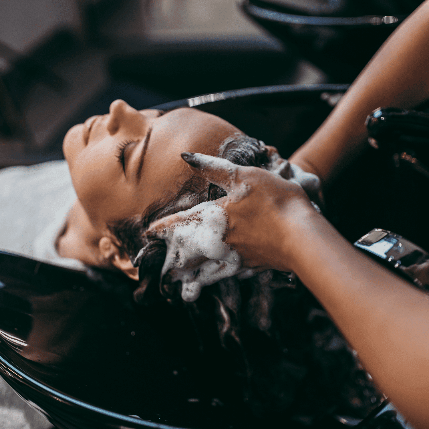 Person receiving a relaxing hair wash at a salon, hands massaging shampoo into scalp.